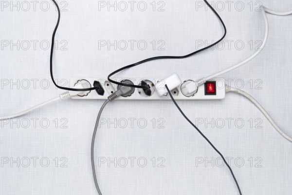 Top view of a power strip with on/off switch and various plugged-in plugs and cables on a white