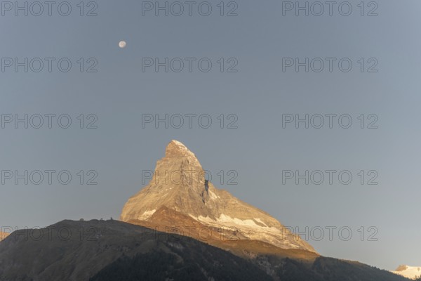The iconic Matterhorn stands high above a clear evening sky illuminated by a bright moon. This
