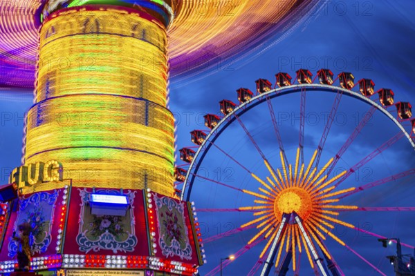 Illuminated chain carousel in motion, behind the Ferris wheel at standstill, Festwiese,
