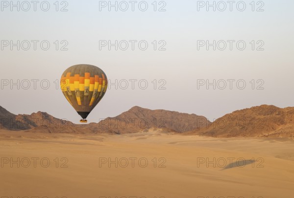 The hot-air balloon above an arid plain and isolated mountain ridges at the edge of the Namib