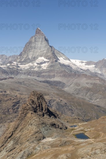 The towering peak of the Matterhorn dominates the clear sky, surrounded by rocky terrain and