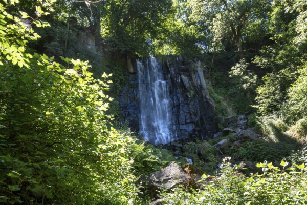 Vaucoux waterfall cascades gracefully over dark rocks, surrounded by lush greenery, Auvergne