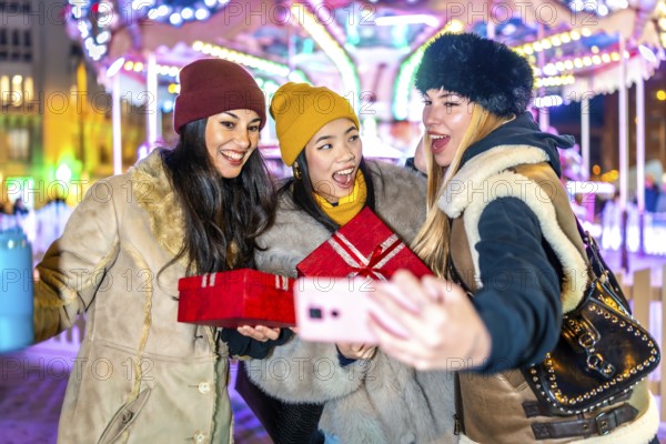 Three happy women holding christmas gifts and taking a selfie at the christmas market with a