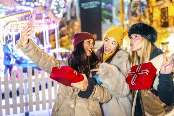 Three happy female friends are taking a selfie holding christmas gifts at a christmas market,