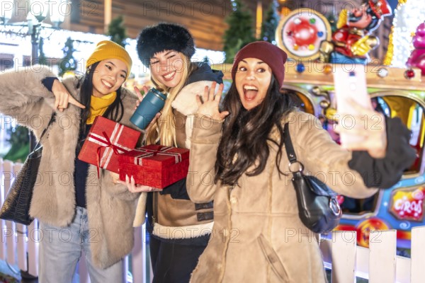 Three happy women taking a selfie at christmas market, holding presents and enjoying winter