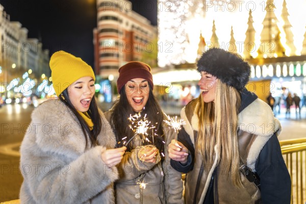Three happy young women holding burning sparklers, enjoying christmas night in a brightly