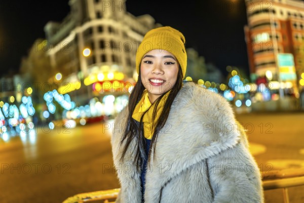 Asian woman wearing cozy winter clothes, smiling and enjoying the vibrant christmas lights