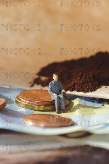Miniature figure of a man sitting on coins and banknotes, ground coffee in a filter bag in the