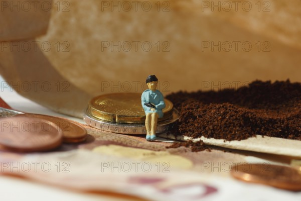 Miniature figure of a woman sitting on coins and banknotes, ground coffee in a filter bag in the