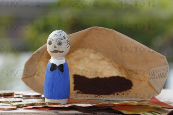 Male wooden cone figure with coins and banknote in front of filter bag with coffee North