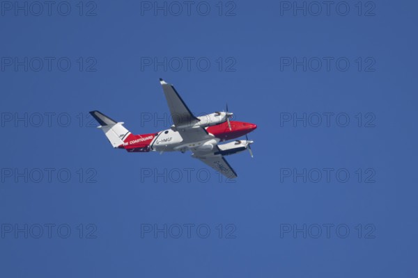 Beech King Air 350 light aircraft of the UK HM Coastguard flying in a blue sky, England, United