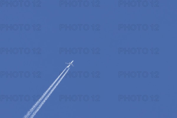 Jet passenger aircraft with a vapour trail or contrail flying in a blue sky, England, United