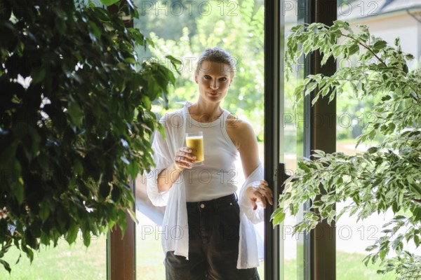 A woman stands in a doorway holding a glass of refreshing beverage. Sunlight filters through