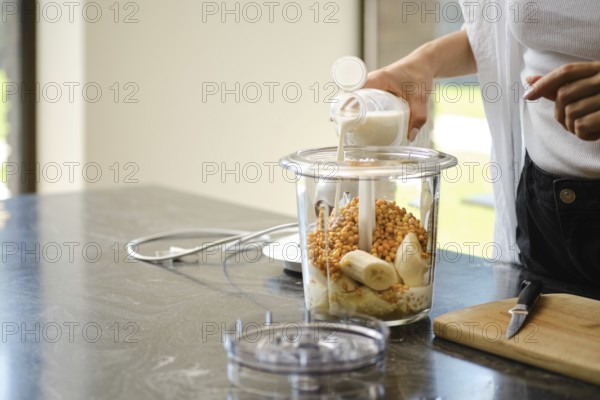 Ingredients are being added to a blender for smoothies. A person is pouring milk into the container
