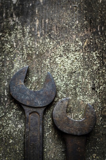 Two old, rusty wrenches rest side by side on a weathered wooden surface, highlighting their wear