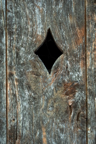 A close-up view of a weathered wooden panel, featuring a diamond-shaped opening cut into the