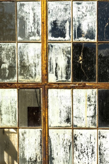 Cracked and peeling window panes reflect light and nearby objects, creating an atmosphere of