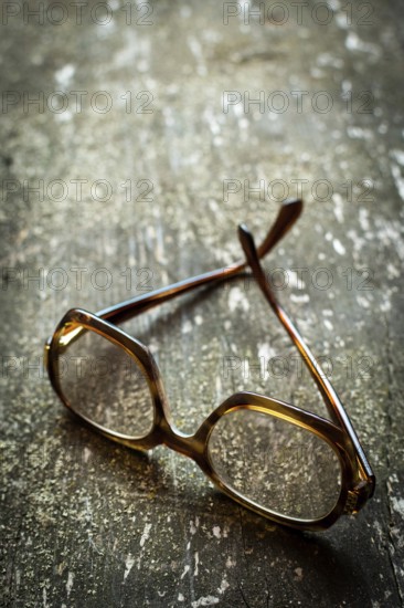 A pair of vintage glasses lies on a weathered wooden surface, enhanced by warm natural light