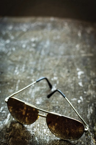 Sleek sunglasses rest on a weathered wooden surface, reflecting softly diffused light. The