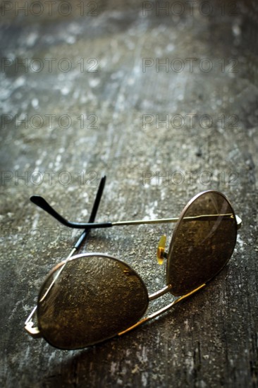 A pair of sunglasses lies on a rustic textured surface, capturing the essence of time. Warm light