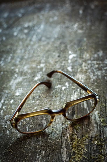 A pair of vintage glasses lies on a weathered wooden table. The unique design is illuminated by