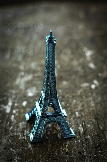 A striking teal miniature Eiffel Tower stands on a rustic wooden surface, bathed in soft lighting