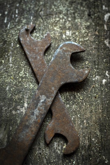 Two old wrenches rest crossed on a weathered wood surface, revealing their rust and signs of many