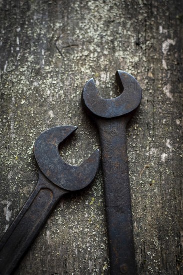 Close-up of two old, rusted wrenches on a wooden workbench, revealing their unique shapes and