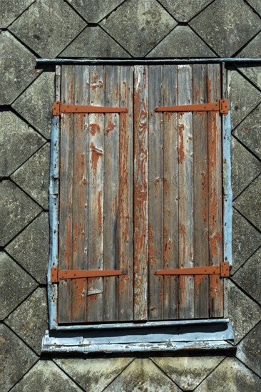 Closed wooden shutters with peeling paint rest against an aged building, highlighting the rustic