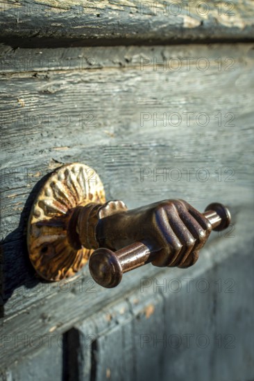A distinctive door handle resembling a hand grips a rustic wooden door, featuring intricate details