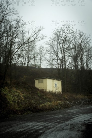 A small yellow building stands alone atop a dark hill, surrounded by bare trees. The atmosphere is