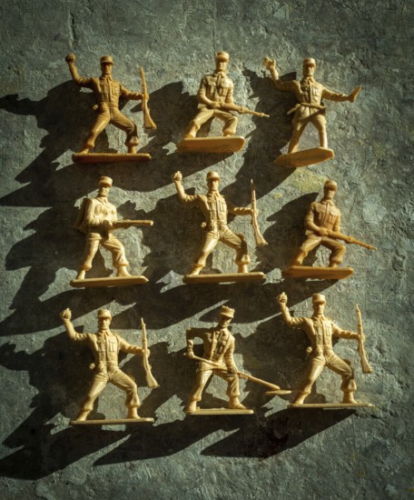 Plastic toy soldiers are displayed in different action poses on a textured surface, casting shadows
