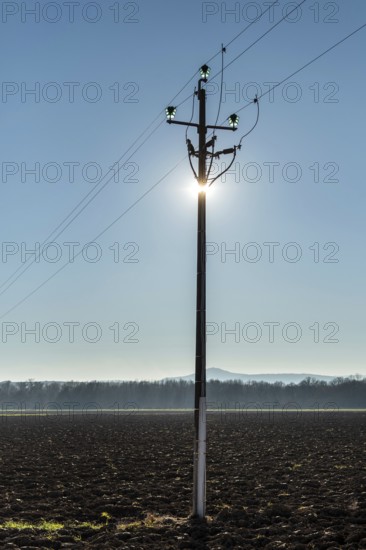 A power pole stands tall in the foreground, with sunlight shining directly behind it, creating a