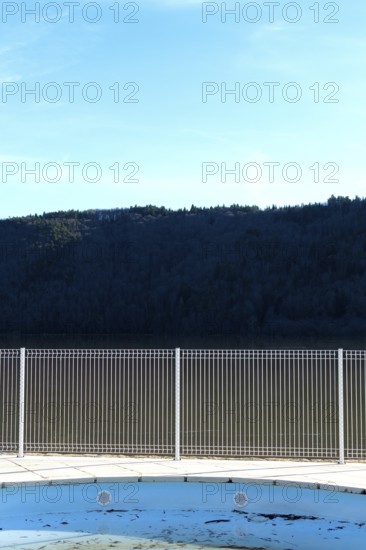 A swimming pool reflects the blue sky and surrounding mountains. A metal fence surrounds the space,