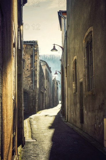 A narrow cobblestone street in an ancient village reflects the soft morning light and shadow. The