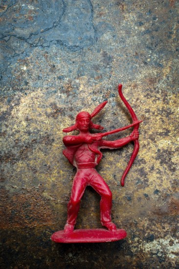 A red plastic toy archer represents a Native American figure, posed with a bow and arrow on a