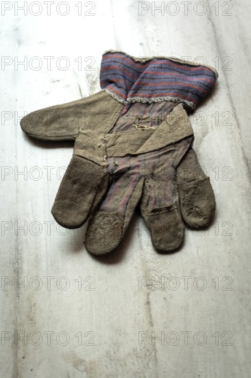 A leather glove, showing signs of age and wear, is placed flat on a textured wooden surface. The
