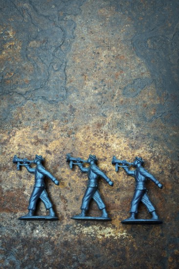 Three small blue toy soldiers are positioned on a rough, textured surface, representing scenes from