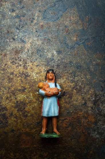 A vibrant plastic figure represents an Indian Native American woman cradling a child, positioned on