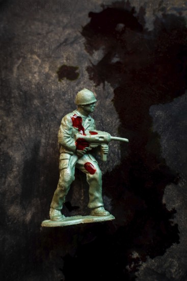 A green soldier figurine holds an assault weapon while displaying battle wounds marked by red