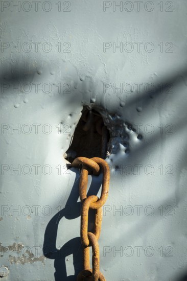 A rusty chain is situated through a weathered hole in a blue surface, with sunlight creating