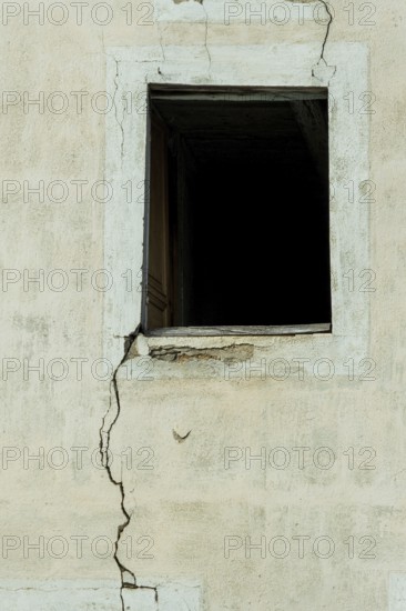A cracked wall features an empty window opening, creating a stark contrast against the faded