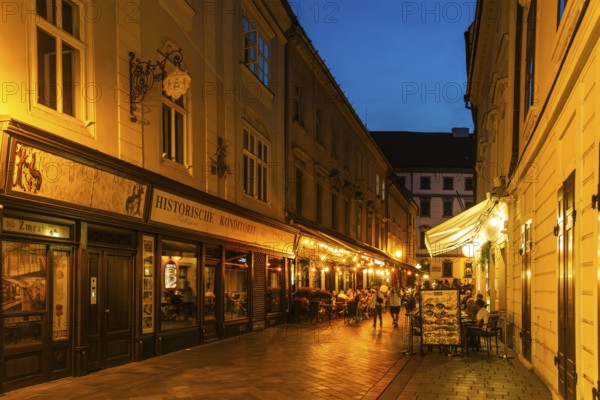 Cosy alley in the old town with illuminated cafés and historic pastry shop in Bratislava, Slovakia