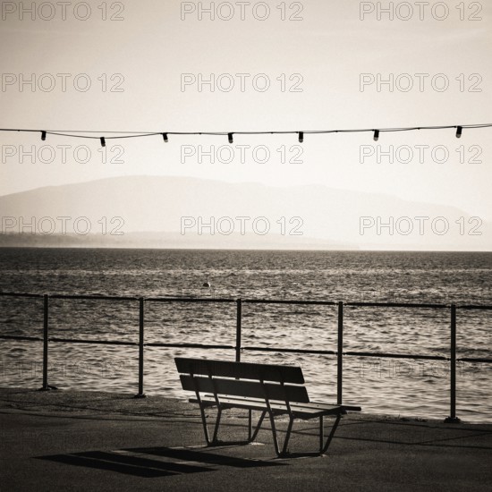 A solitary bench sits by the lakeside promenade in Nyon, Switzerland. Gentle waves ripple in Geneva