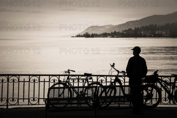 A tourist stands at the edge of Lake Geneva, captivated by the serene waters and distant hills.