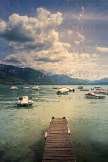 A wooden pontoon extends over the tranquil waters of Annecy Lake, surrounded by mountains and