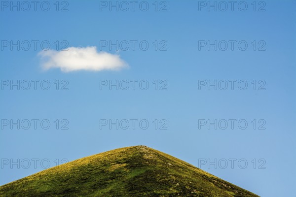 A solitary cloud floats above a green mountain in the Auvergne-Rhone-Alpes region of France. The