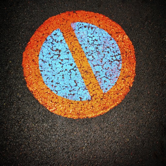 A vibrant no parking symbol is prominently displayed on a black asphalt surface, featuring a blue