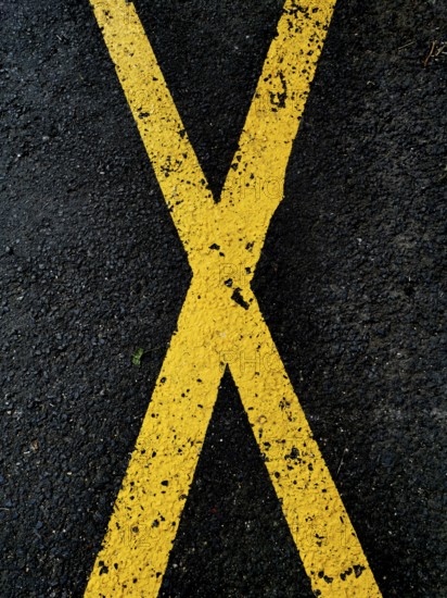 A pattern of yellow crossing lines painted on a dark asphalt surface emphasizes a bold visual