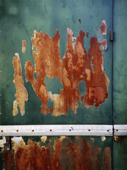 A weathered green metal surface displays extensive rust patches and peeling paint, highlighting the